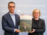 Bundesminister Özdemir und Nicole Wellbrock halten zusammen den Ausdruck des Waldzustandsberichts 2023