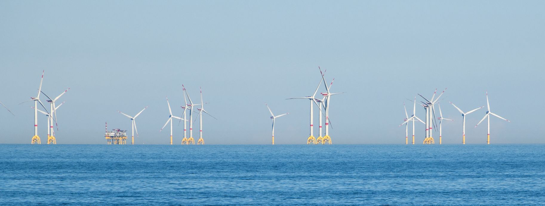 Mehrere Windkrafträder auf offener See mit einer Versorgungstation