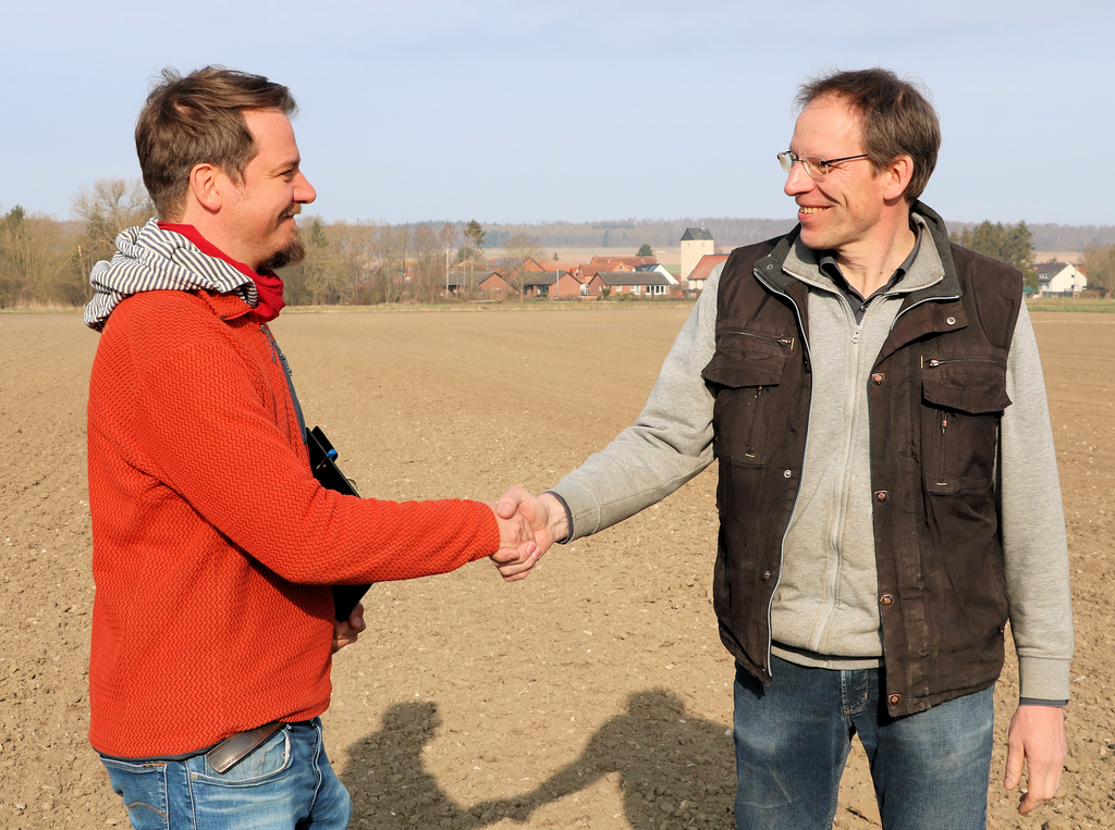The photo shows a handshake between Christopher Poeplau and a farmer.