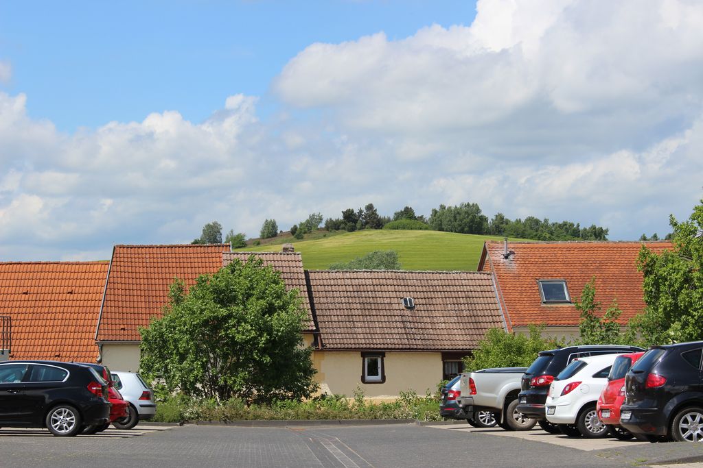 Häuser am Ortsrand einer ländlichen Kleinstadt mit einem Parkplatz voller Autos.