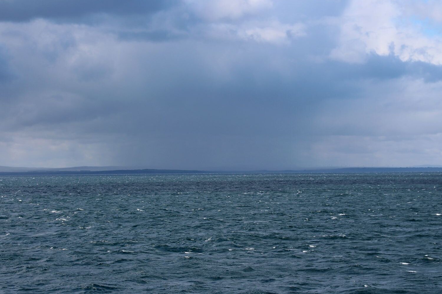 Blick auf das Meer mit dunklen Wolken und am Horizont ist Land zu sehen.