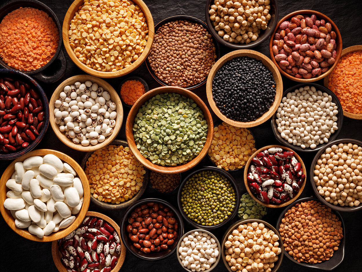 Hülsenfrüchte, ein Set bestehend aus verschiedenen Arten von Bohnen, Linsen und Erbsen auf schwarzem Hintergrund, Ansicht von oben.