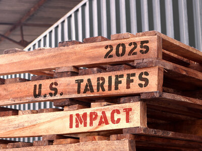 Auf eine Palette ist in Großbuchstaben auf englisch geschrieben: 2025 US Zölle Einfluss