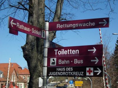 Schilder als Richtungsweiser in verschiedene Richtungen unter anderem zur Toilette, zu Bus und Bahn und zum Rathaus