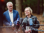 Two people stand in front of microphones in the forest