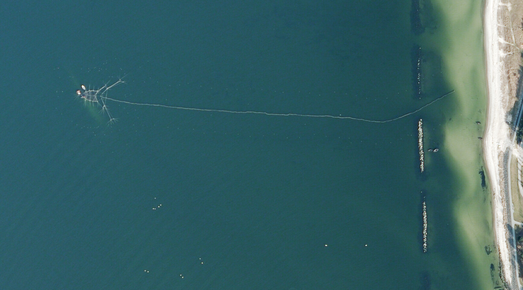 Luftaufnahme einer langen Kumreuse im Meer nahe einer sandigen Küste.