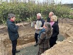 Fünf Personen, die in einer Boden-Profilgrube stehen. Eine Person erklärt etwas. Im Hintergrund sind Pflanzen zu sehen.