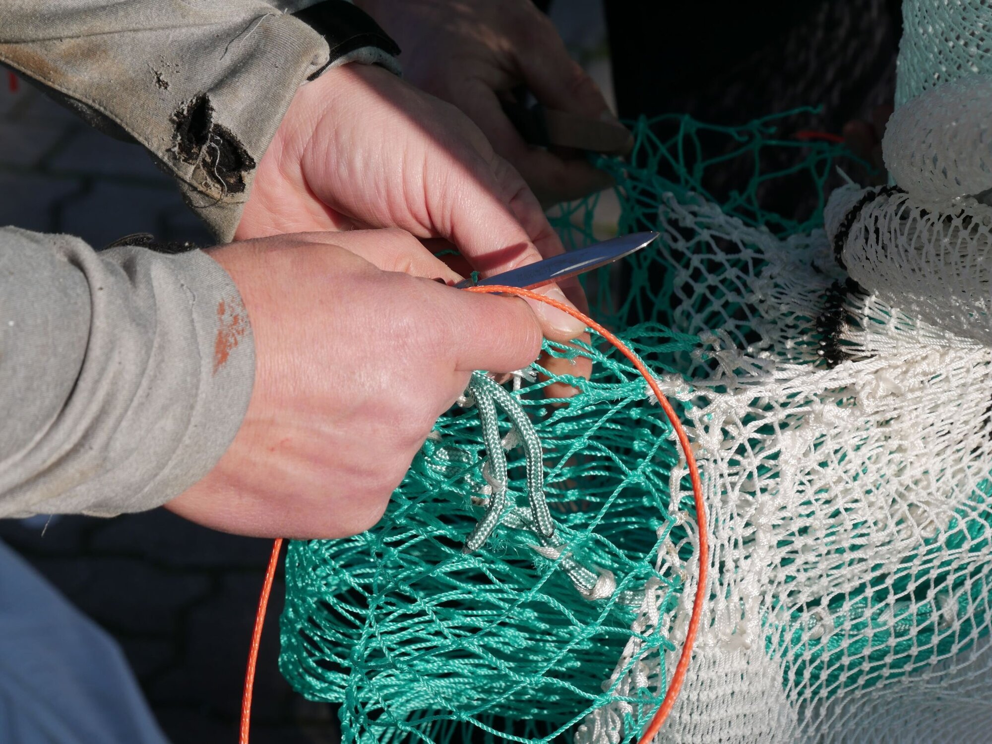 Letzte Netzarbeiten an der Auslassöffnung vom Siebnetz. Detailaufnahme von Händen, die am Netz arbeiten
