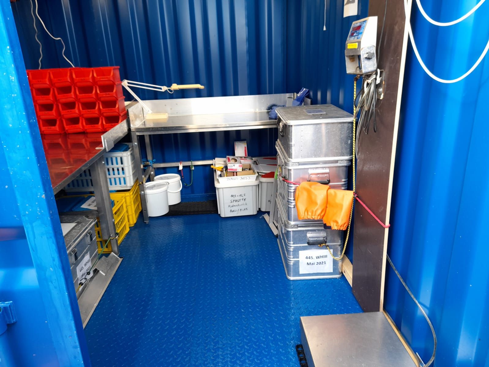 Ein blauer Container mit Metalltischen, Kisten und einigem Arbeitsmaterial