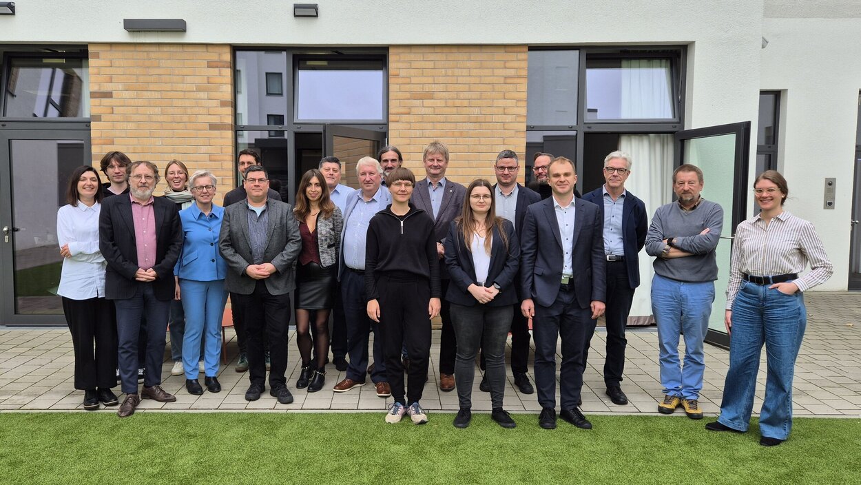 20 Wissenschaftler:innen vor einem Konferenzgebäude