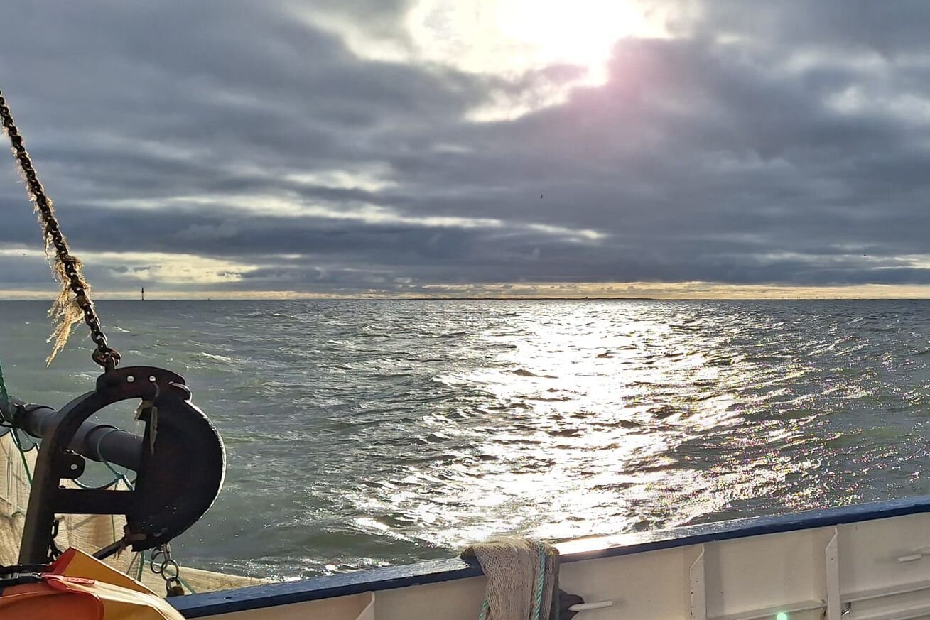 Die Sonne malt einen hellen Streifen auf das Meer. Die Sonne erhellt einen Streifen des dunkelgrauen Meeres.