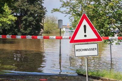 Ein Achtung Hochwasser Schild vor einem überfluteten Weg