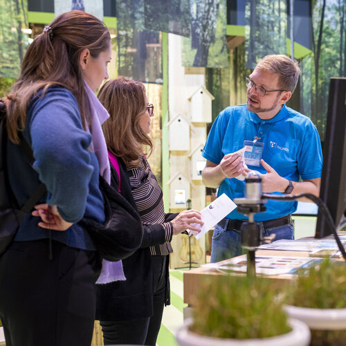 240119_IBMEL_PHT11.JPG Drei Personen im Gespräch an einem Messestand