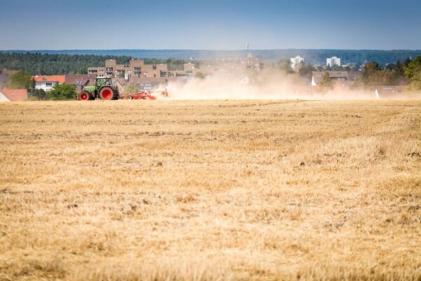 Stoppelfeld Stoppelfeld mit einer Landwirschaftlichen Maschine, die eine große Staufahne hinter sich her zieht