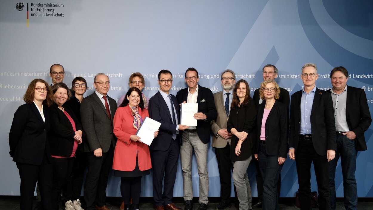 Bundesminister Özdemir mit den Mitgliedern des Wissenschaftlichen Beirates vor der Pressewand, in den Händen hält er die Stellungnahme Menschengruppe: Beirat übergibt Stellungnahme „Ernährungsarmut unter Pandemiebedingungen“