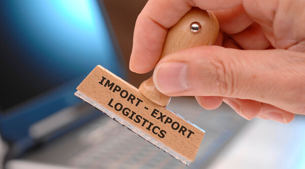 Die aktuelle Zollpolitik entspringt einer vermeintlich unfairen Handelsbilanz. Ein Holzstempel mit der Aufschrift Export, Import, Logistics.