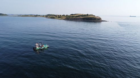 Kleines Arbeitsboot ankert vor einer Insel mit Klippe