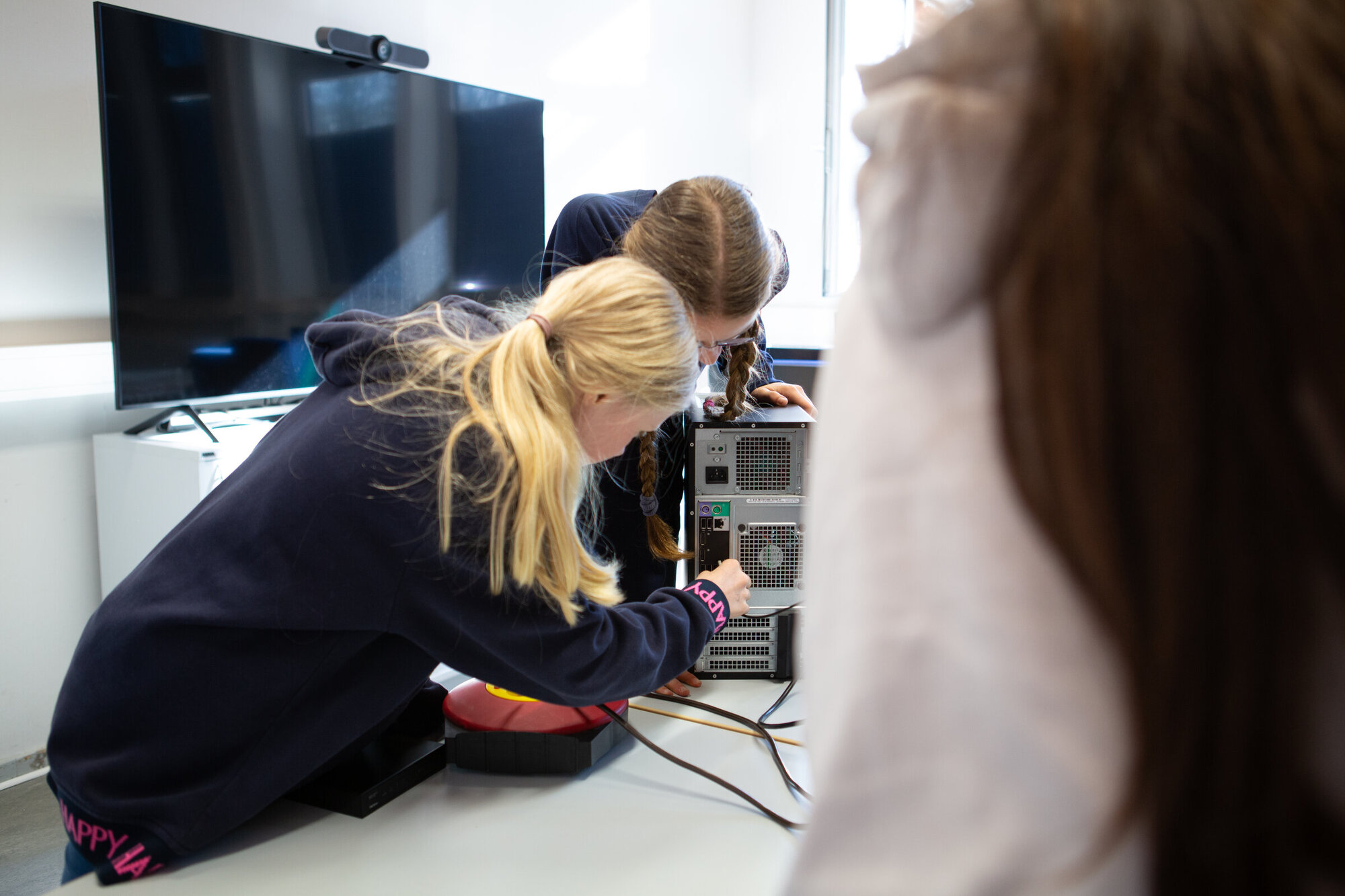 Zwei Mädchen beugen sich über das Innenleben eines Computers. Eine von ihnen schraubt mit einem Schraubendreher.
