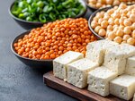 Schüsseln mit Hülsenfrüchten und Tofuquader auf einem Holzbrett.