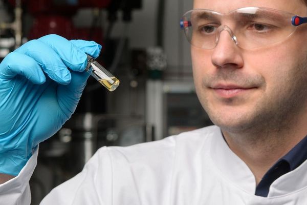 Eine Person in Laborschutzausrüstung schaut auf ein kleines Glasröhrchen mit Flüssigkeit