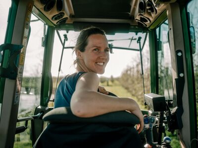 Eine Frau sitzt auf dem Fahrersitz eines Teckers und schaut nach hinten aus dem Fenster.