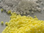 Fertiliser pellets in white and yellow on a light-coloured flat base.