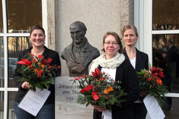 Die drei Damen stehen neben der Büste vom Johann Heinrich von Thünen und halten Ihre Urkunden und einen Blumenstrauss.