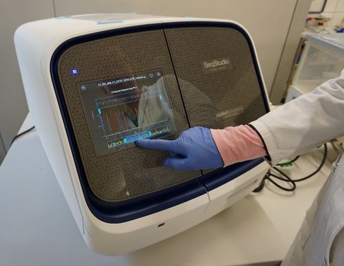 Das Gerät "ABI Seqstudio" ist eingeschaltet und wird von einer Person, dessen Arm nur zu sehen ist, mit blauen Laborhandschuhen bedient.
