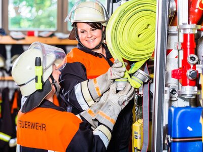 Feuerwehrfrauen verladen Schläuche in das Einsatzfahrzeug.