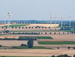 Inmitten von vielen gelbbraunen Feldern und einigen Bäumen stehen große Windräder
