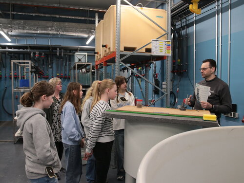Mehrere Kinder vor einem runden Fischbecken mit einer Person die erklärt.