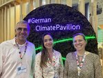 Three people are standing next to each other in front of the #German Climate Pavilion sign.