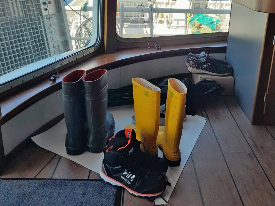 Gummistiefel und Schuhe stehen vor einem Fenster an Bord