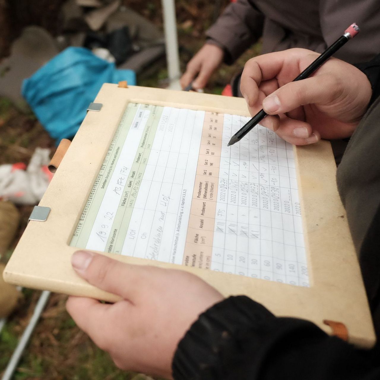 Datenaufnahme während der Feldarbeit. Die Daten zu den Bodenuntersuchungen werden auf einem Protokoll notiert, welches in ein Klemmbrett gespannt ist.