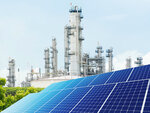 Eine Photovoltaikanlage im Vordergrund und eine Fabrikanlage im Hintergrund.