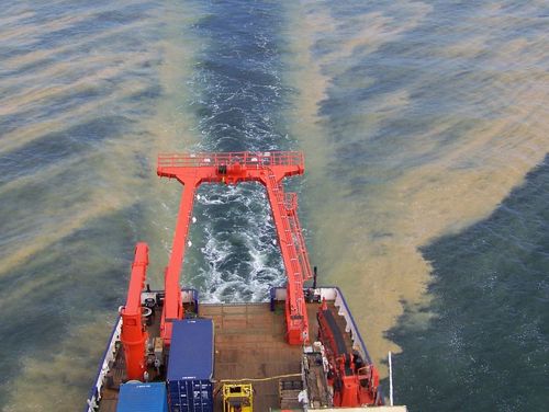 View from above of a ship's deck and a huge brown patch of blue-green algae on the water 