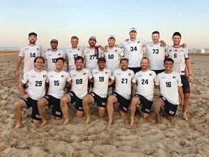 Fifteen people wearing white jerseys stand in two rows on the sand.