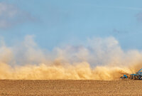 Trockene, wenig bedeckte Böden sind besonders anfällig für Erosion. Traktor, der den Boden mit Scheibenegge bearbeitet und eine riesige gelbe Staubwolke verursacht.