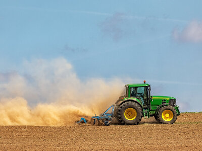 Tractor working the soil with a disc harrow, creating a huge yellow cloud of dust.