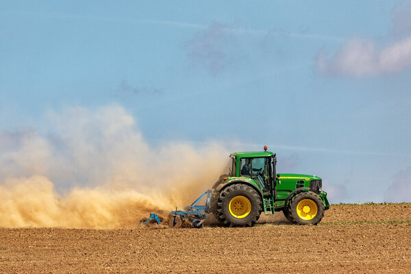 Tractor working the soil with a disc harrow, creating a huge yellow cloud of dust.