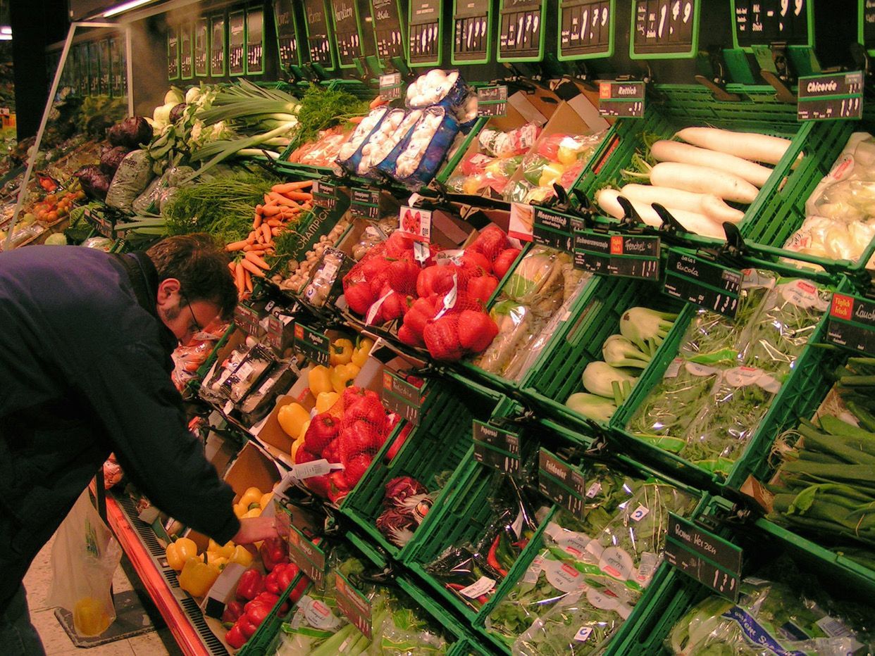 Eine Person beugt sich über die Angebote an Gemüse in einem Supermarkt