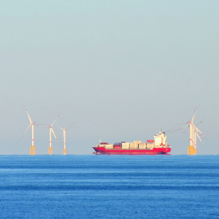 Ein Containerschiff auf offener See zwischen Windrädern