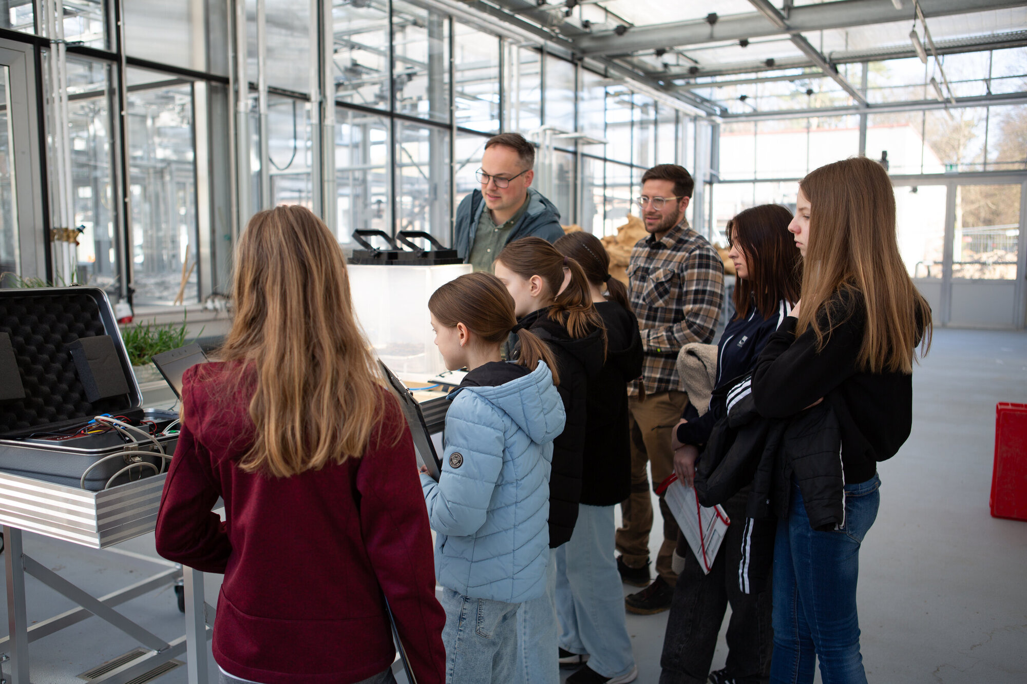 Gruppe von Kindern und Erwachsenen in einem Labor, die an einem Tisch mit technischen Geräten und Pflanzen arbeiten.