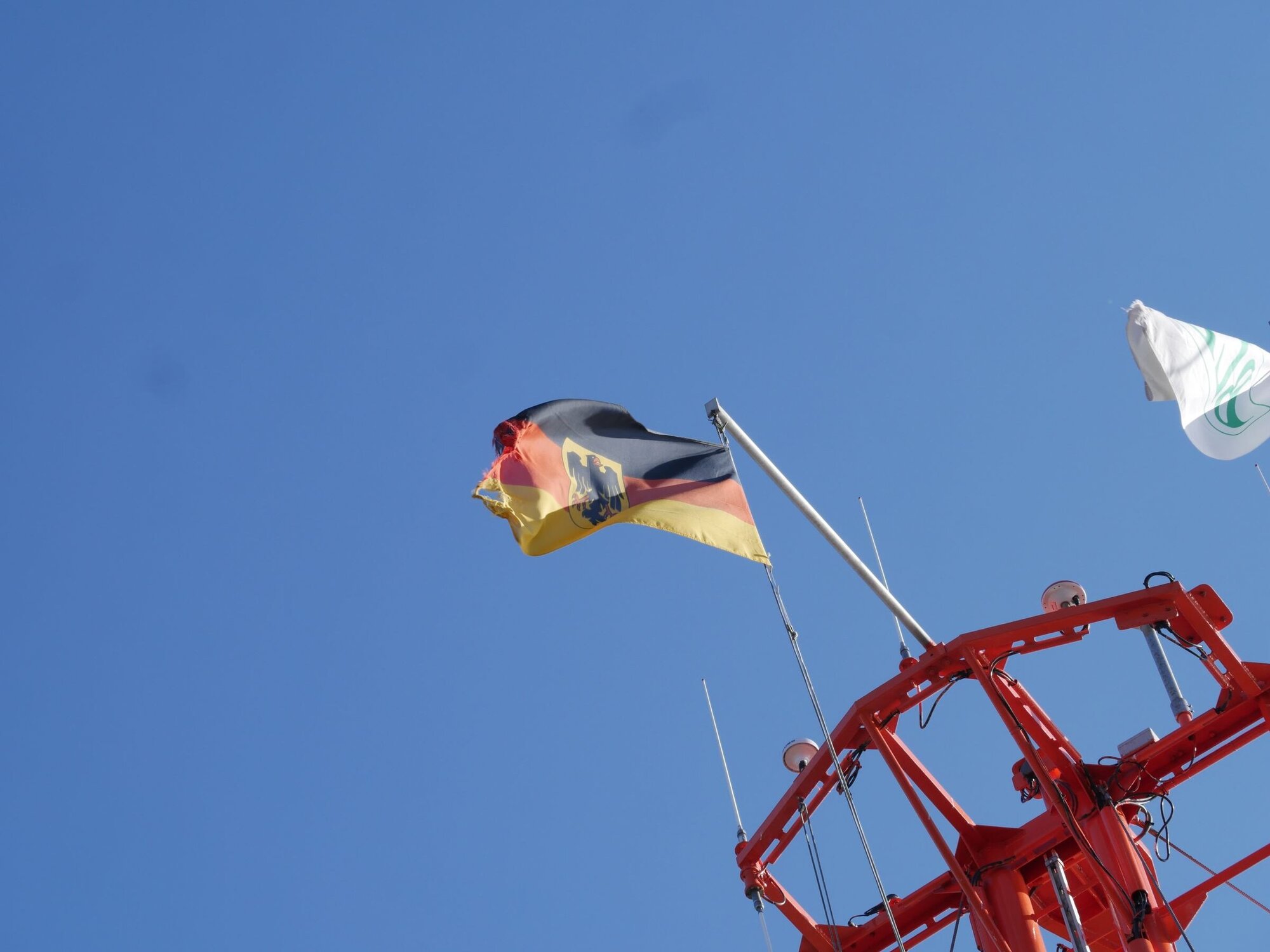 Die Flagge mit Bundesadler weht im Wind. Die Deutschlandfahne weht vor blauem Himmel im Wind
