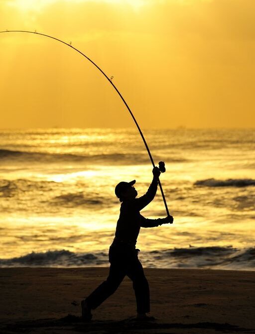 Ein Angler abends am Strand im Gegenlicht
