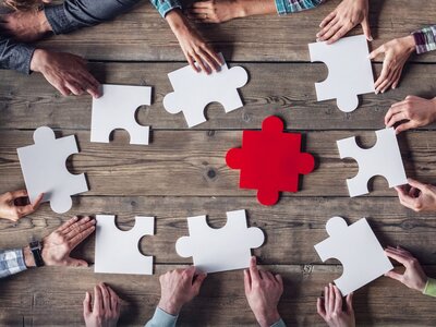 Mehrere Personen sitzen am Tisch und halten Puzzleteile in der Hand um sie zu kombinieren Sie