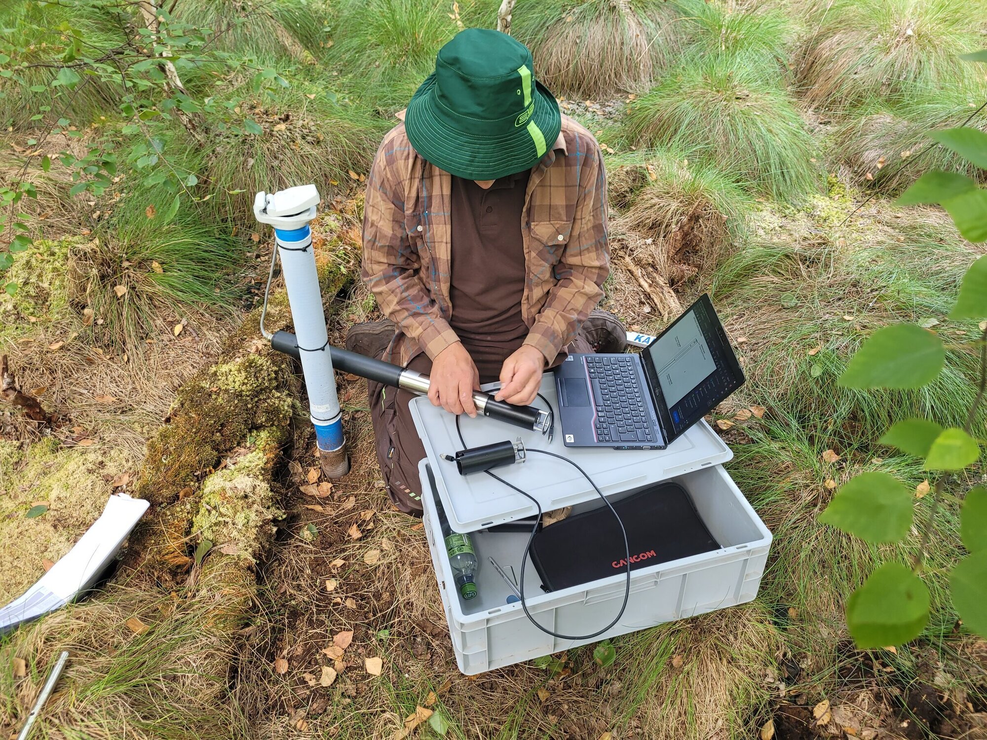 Die Forschenden lesen regelmäßig die Daten der Messstationen aus. Person arbeitet mit Messgeräten und Laptop an einer Moorboden-Messstation im Wald.