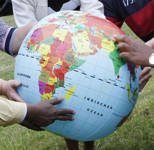 Viele Hände halten eine aufblasbare Weltkugel auf der Afrika zu sehen ist