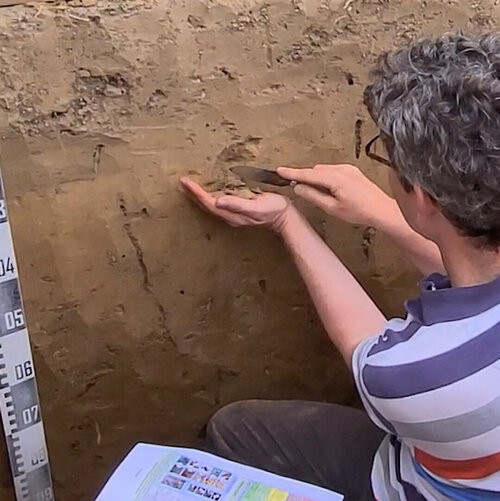 Mann sitzt in einem tiefen Erdloch auf einem Feld und schabt mit einem Messer Erde von der Wand des Lochs
