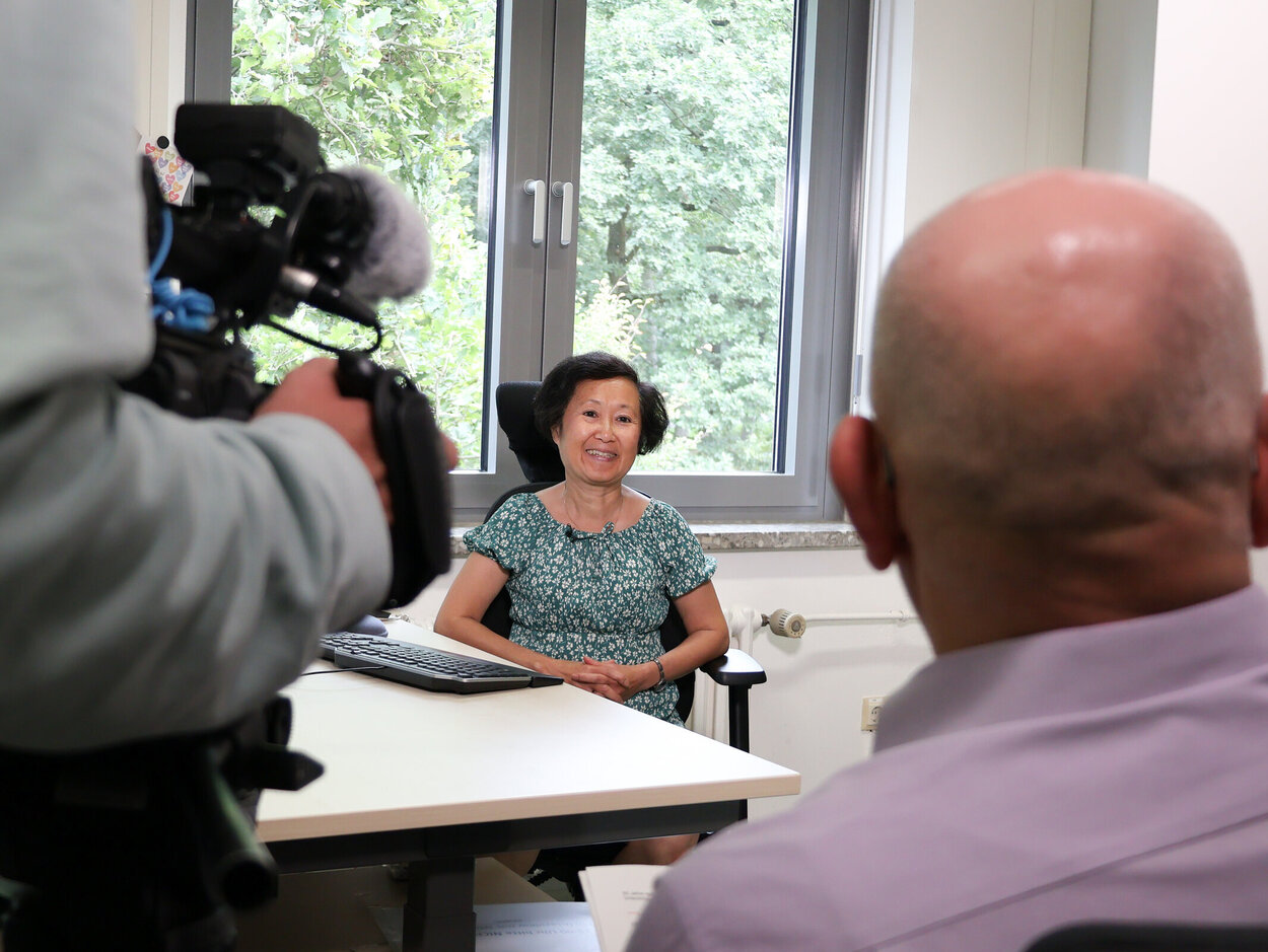Ein Filmteam des NDR besucht Thi Tu Uyen Tran an ihrem Arbeitsplatz. Eine Person wird gefilmt und der Inteviewer ist von hinten zu sehen.